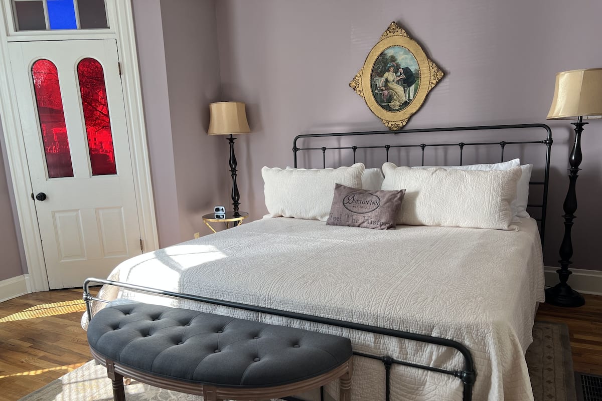 Une chambre à coucher bien rangée, avec un lit, des oreillers, un banc et deux lampes de chevet.
