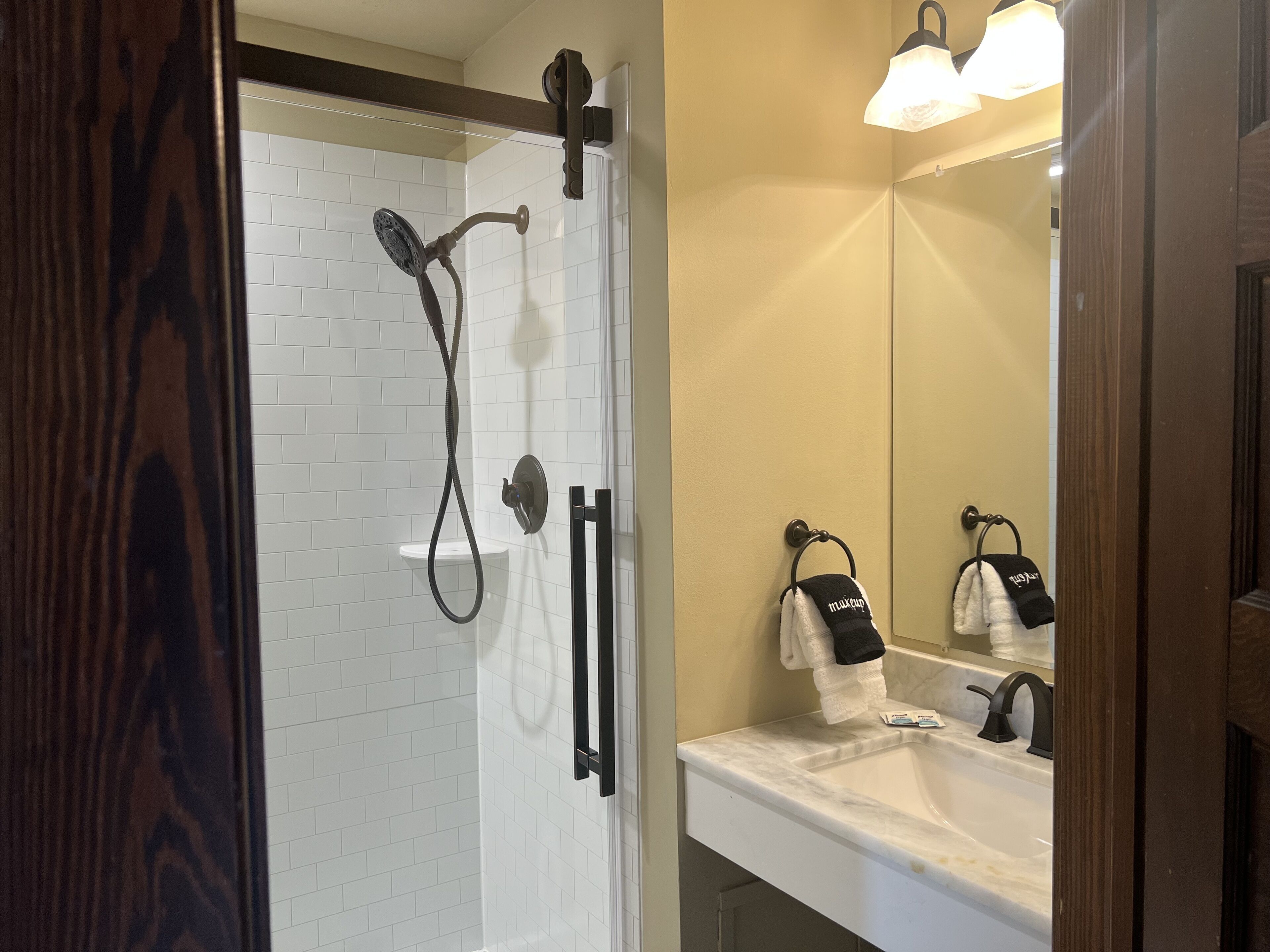 A bathroom with a white tiled shower, a sink with a mirror, and towels hanging on a rack.