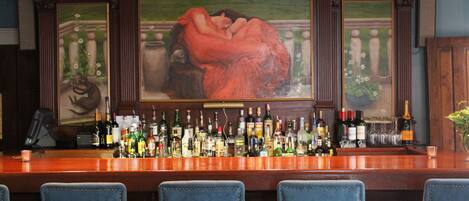 A bar with a long counter displaying various bottles and glasses, flanked by blue upholstered chairs.