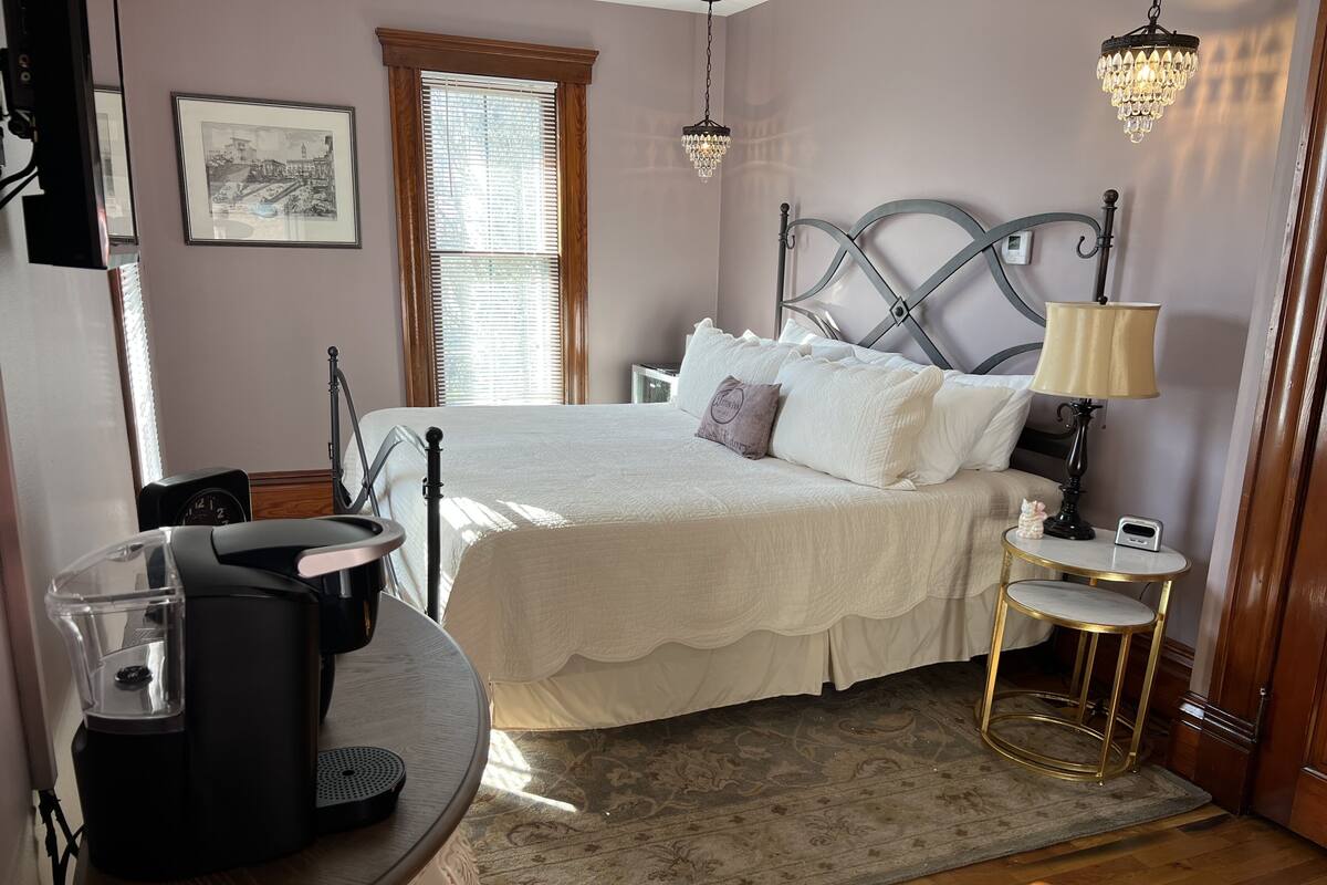 Une chambre à coucher bien rangée, avec un lit, une table de chevet, une lampe et une machine à café.