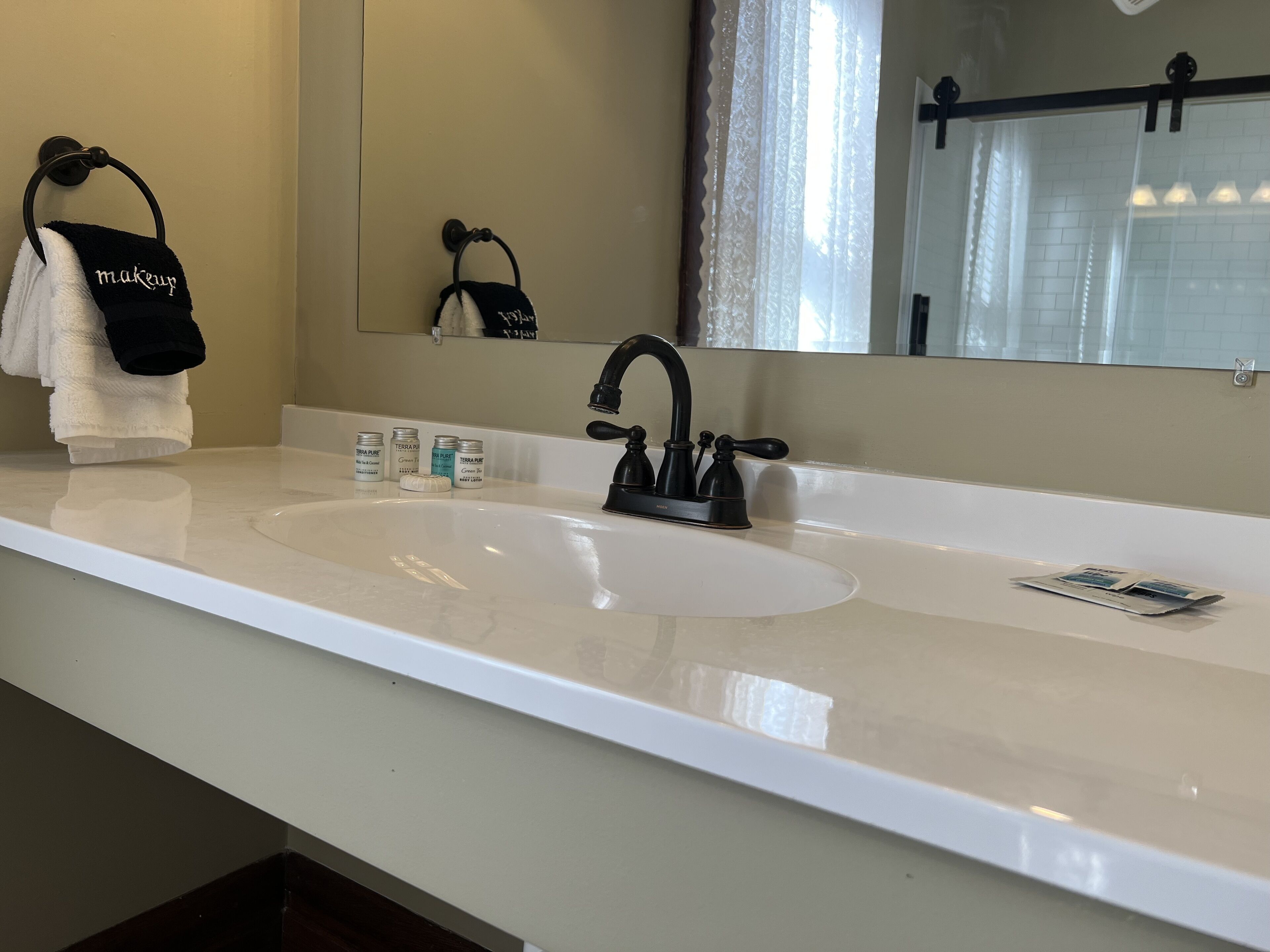 Un baño con lavamanos blanco, grifo negro y un perchero con una toalla que dice 'maquillaje'.
