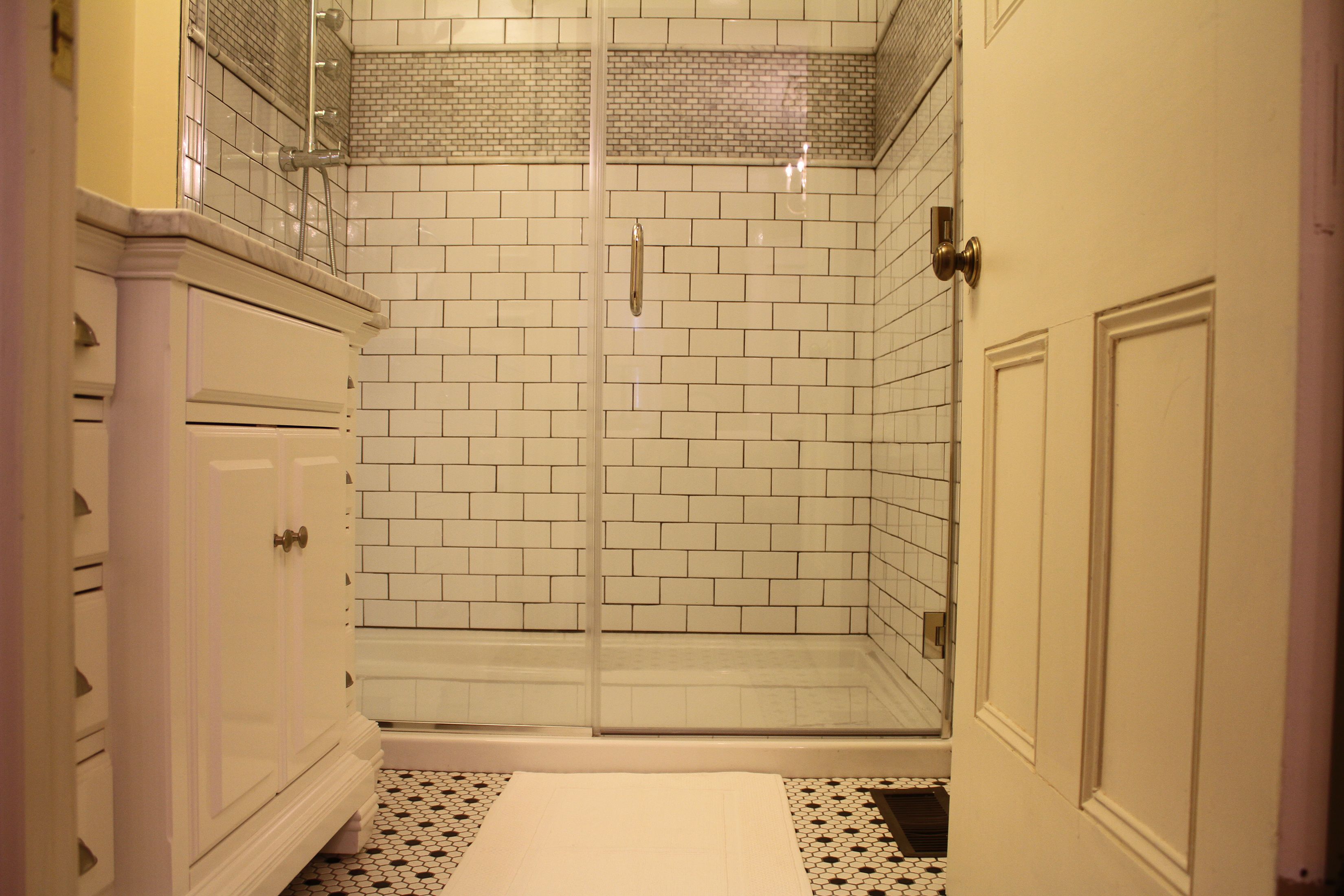 A bathroom with white tiled walls, a glass shower enclosure, and a white vanity with drawers.