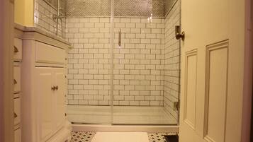 A bathroom with white tiled walls, a glass shower enclosure, and a white vanity with drawers.