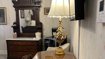 A wooden dining table with a remote control and a book on it. A lamp with a decorative base is on the table. A mirror with a wooden frame is on the wall behind the table.