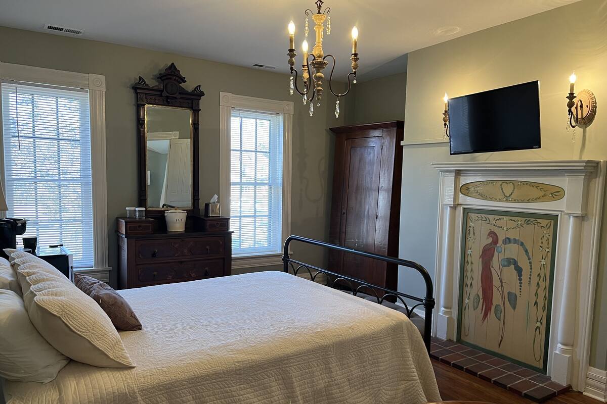 Une chambre à coucher avec un grand lit, une commode, un miroir, un lustre, une cheminée et un téléviseur.