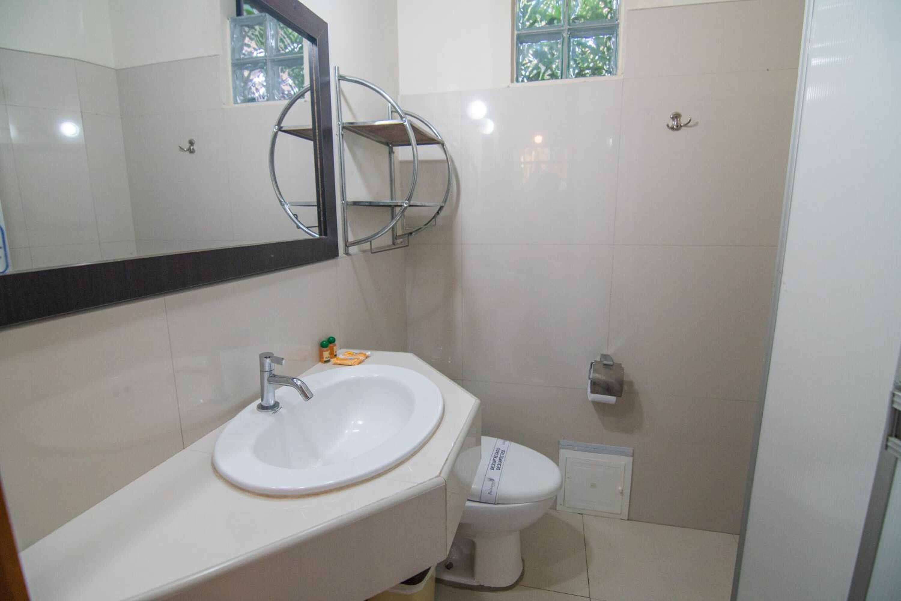 Un baño con lavamanos blanco, un espejo, inodoro y ventana con vista a follaje.