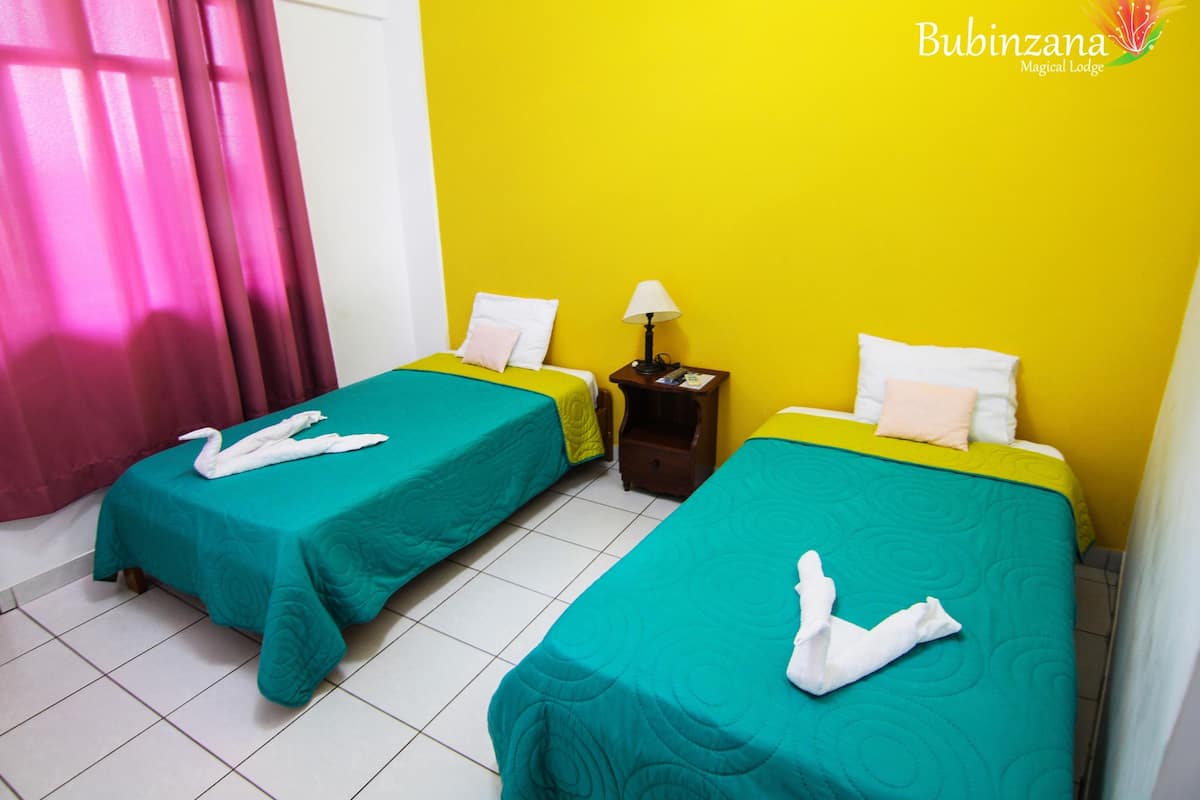 Ein Hotelzimmer mit zwei Betten, jeweils mit türkisfarbenem Bettzeug und weißen Handtüchern, die zu Schwänen geformt sind.