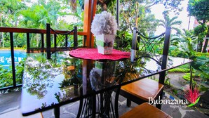 A glass table with a red mat, surrounded by chairs, in a lush green outdoor setting.