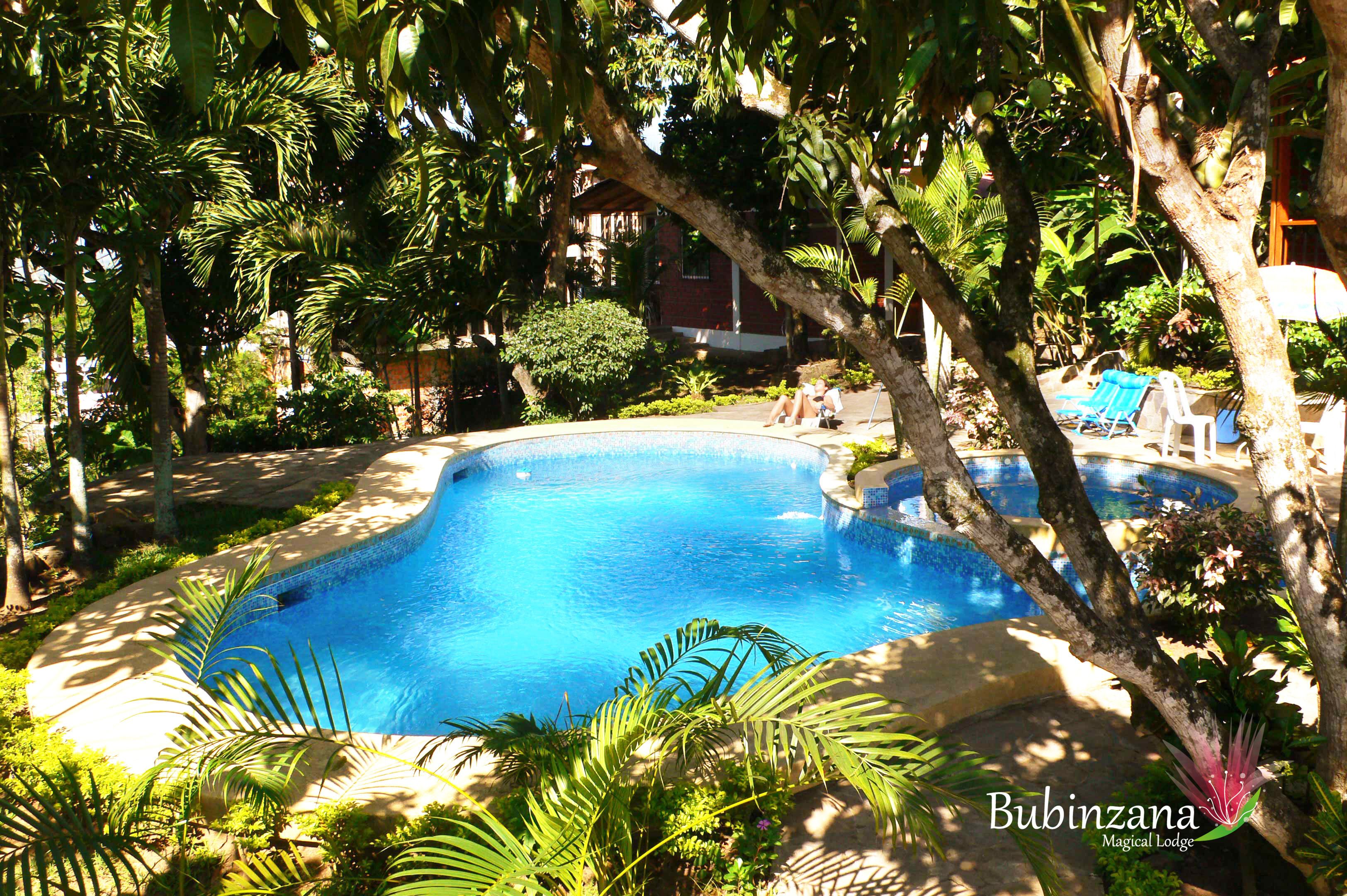 Una piscina rodeada de exuberante vegetación y un edificio al fondo.