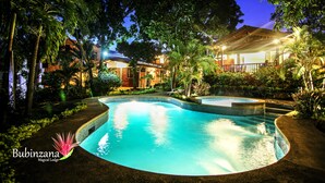 A swimming pool surrounded by lush greenery and a building with a tiled roof.