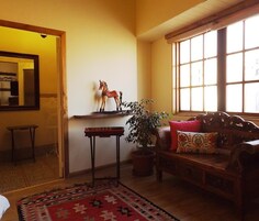 Una sala de estar acogedora con un banco de madera, un tapete rojo estampado, una planta en maceta y una figurita decorativa de un caballo sobre una estantería.