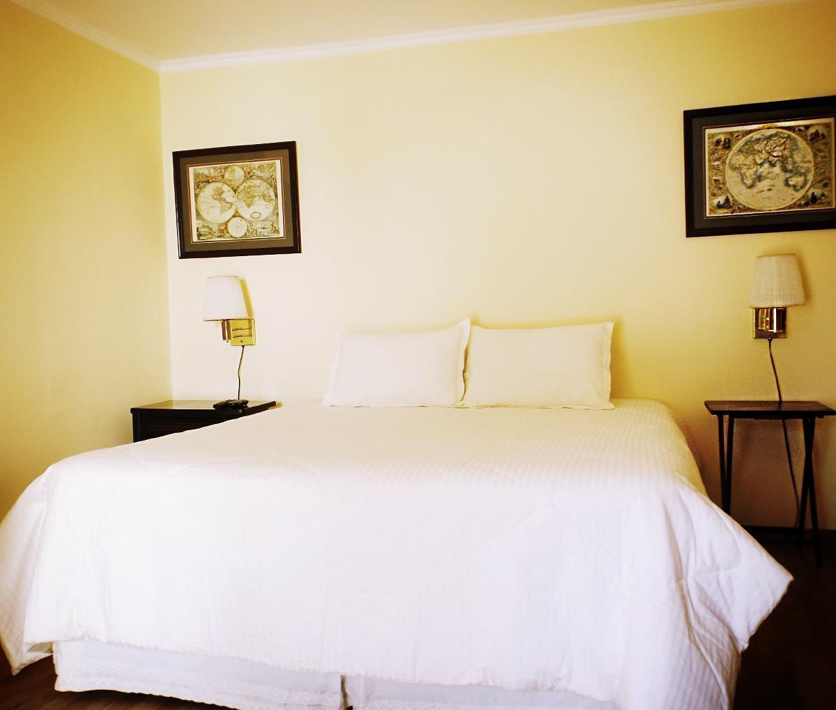 Una habitación de hotel con una cama grande, dos mesitas de noche y dos lámparas de pared.