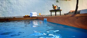 A swimming pool with a wooden deck and a stone wall in the background.