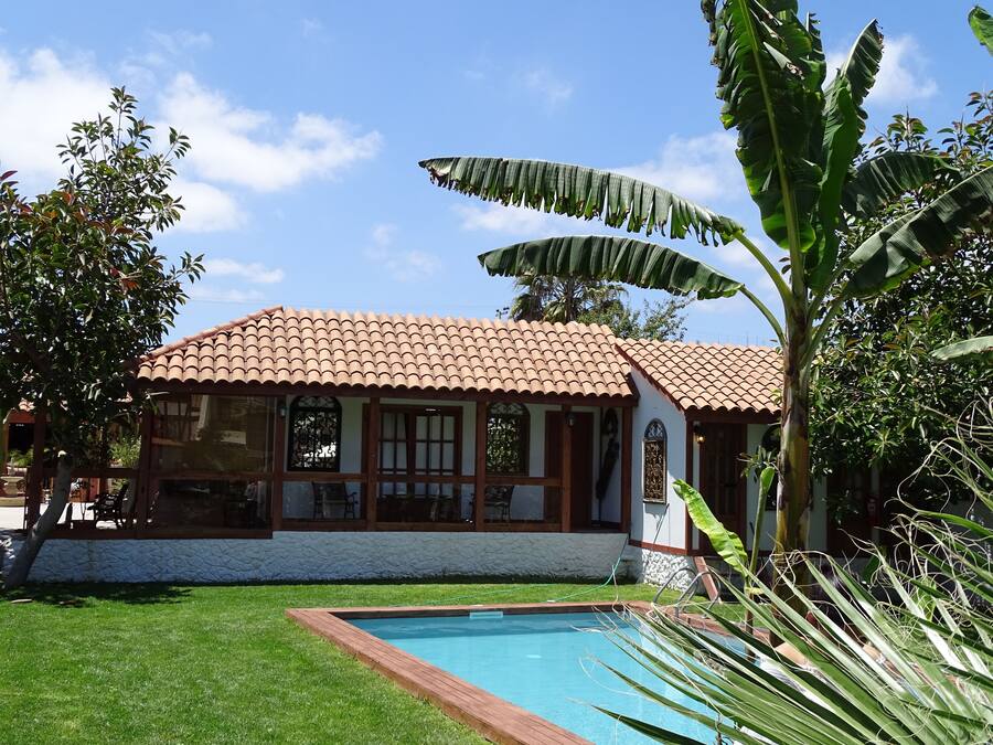 A house with a tiled roof, a swimming pool, and lush greenery.