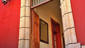 A building entrance with a red facade, a wooden door, and a stone pillar. - Primera Hacienda Hotel Boutique (La Serena)