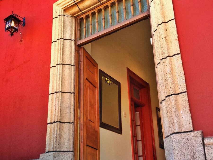 Entrada de un edificio con fachada roja, una puerta de madera y un pilar de piedra.