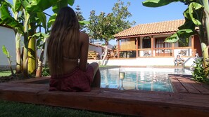 A person sitting by a pool with a house in the background.