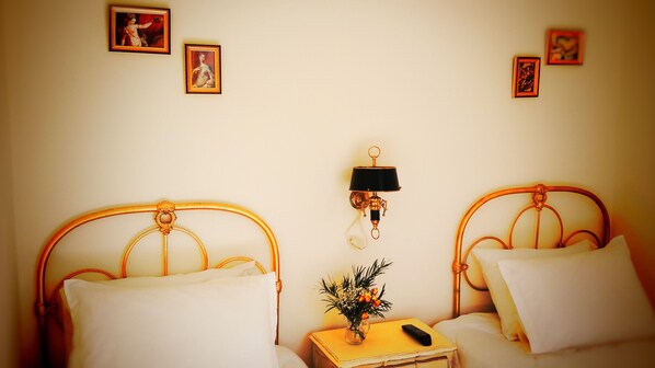 A bedroom with two beds, a nightstand with a vase of flowers, a remote control, and wall-mounted lamps.