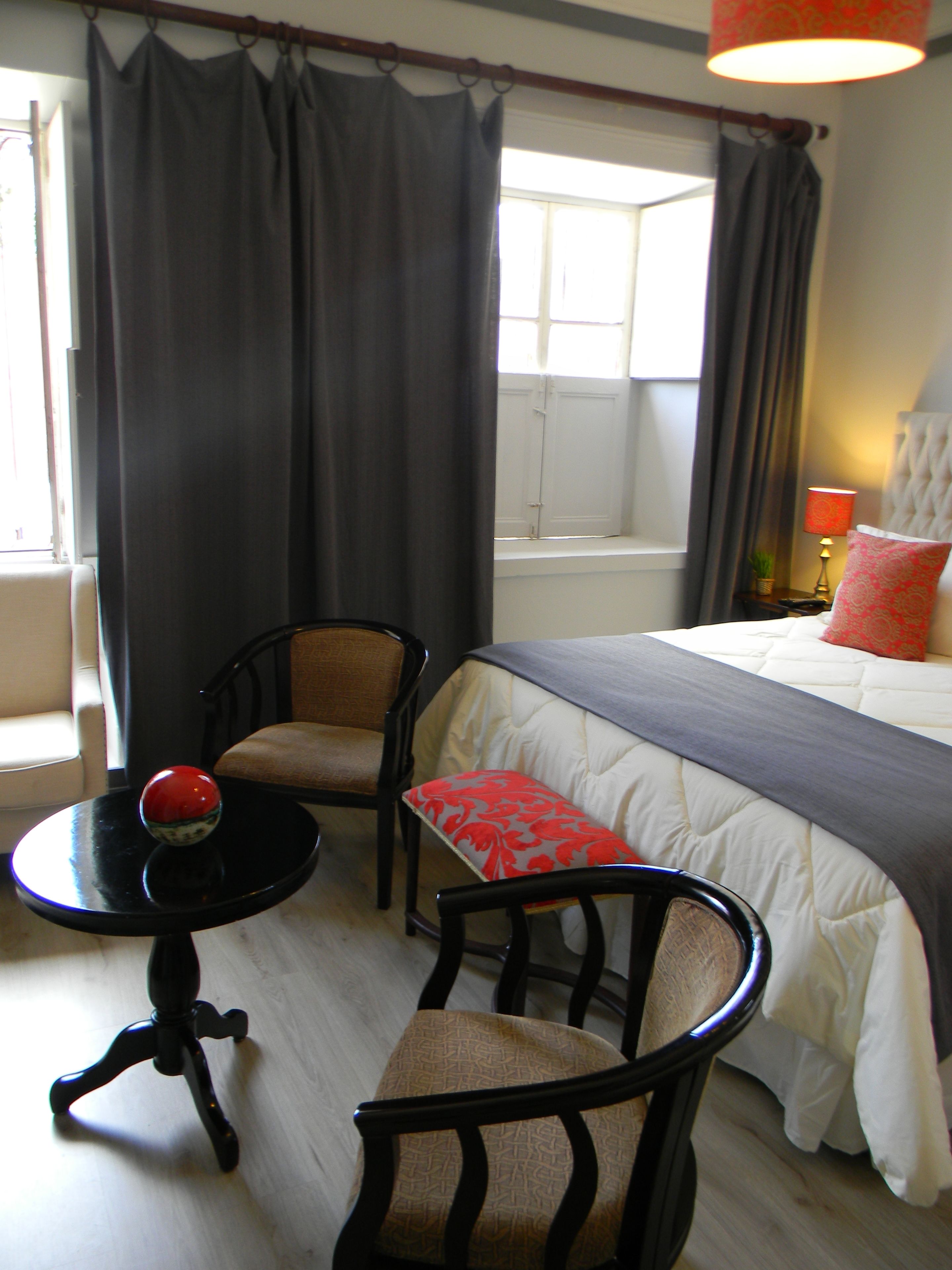 A hotel room with a bed, two chairs, a small table with a red ball, and a window with curtains.