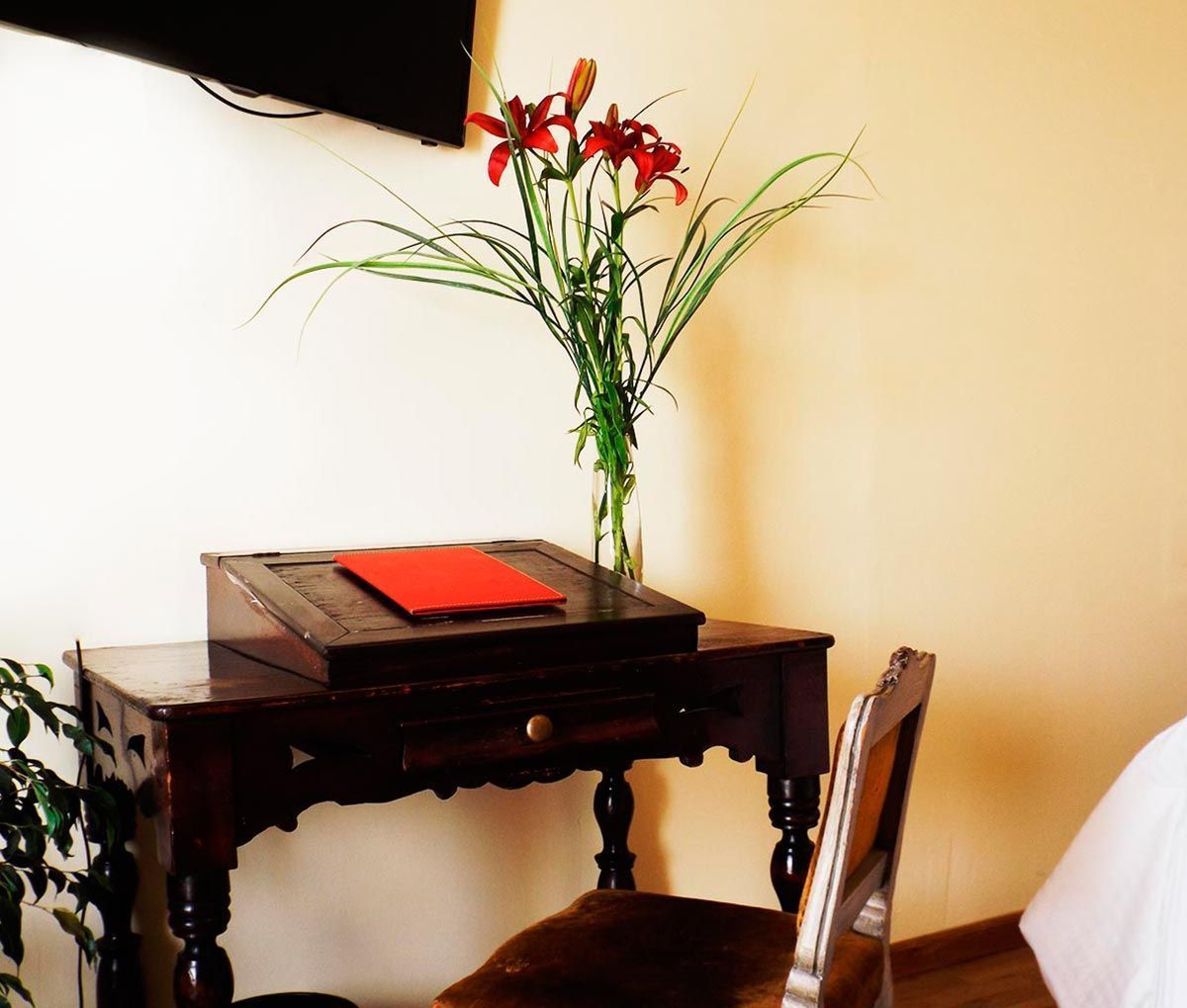 A wooden desk with a red folder, a vase with red flowers, and a chair.