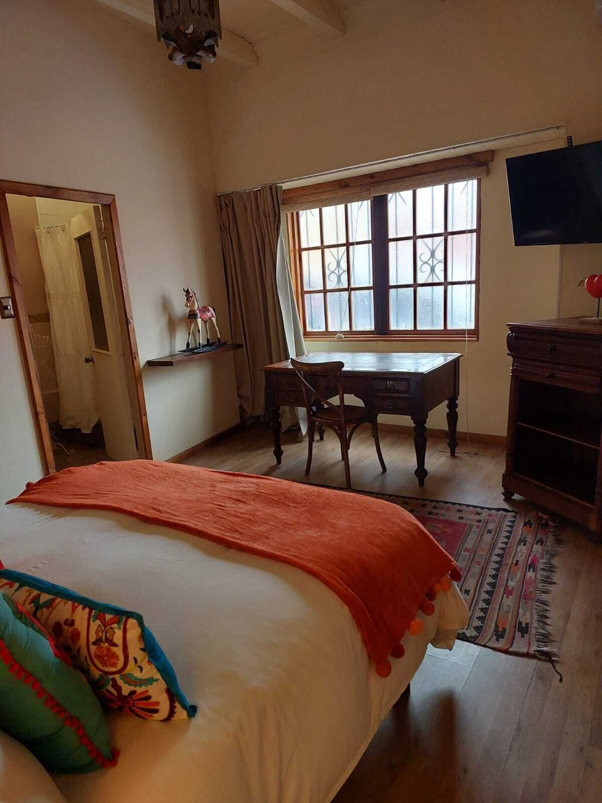 A bedroom with a bed, a desk, a chair, a television, and a window.