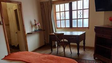 A bedroom with a bed, a desk, a chair, a television, and a window.