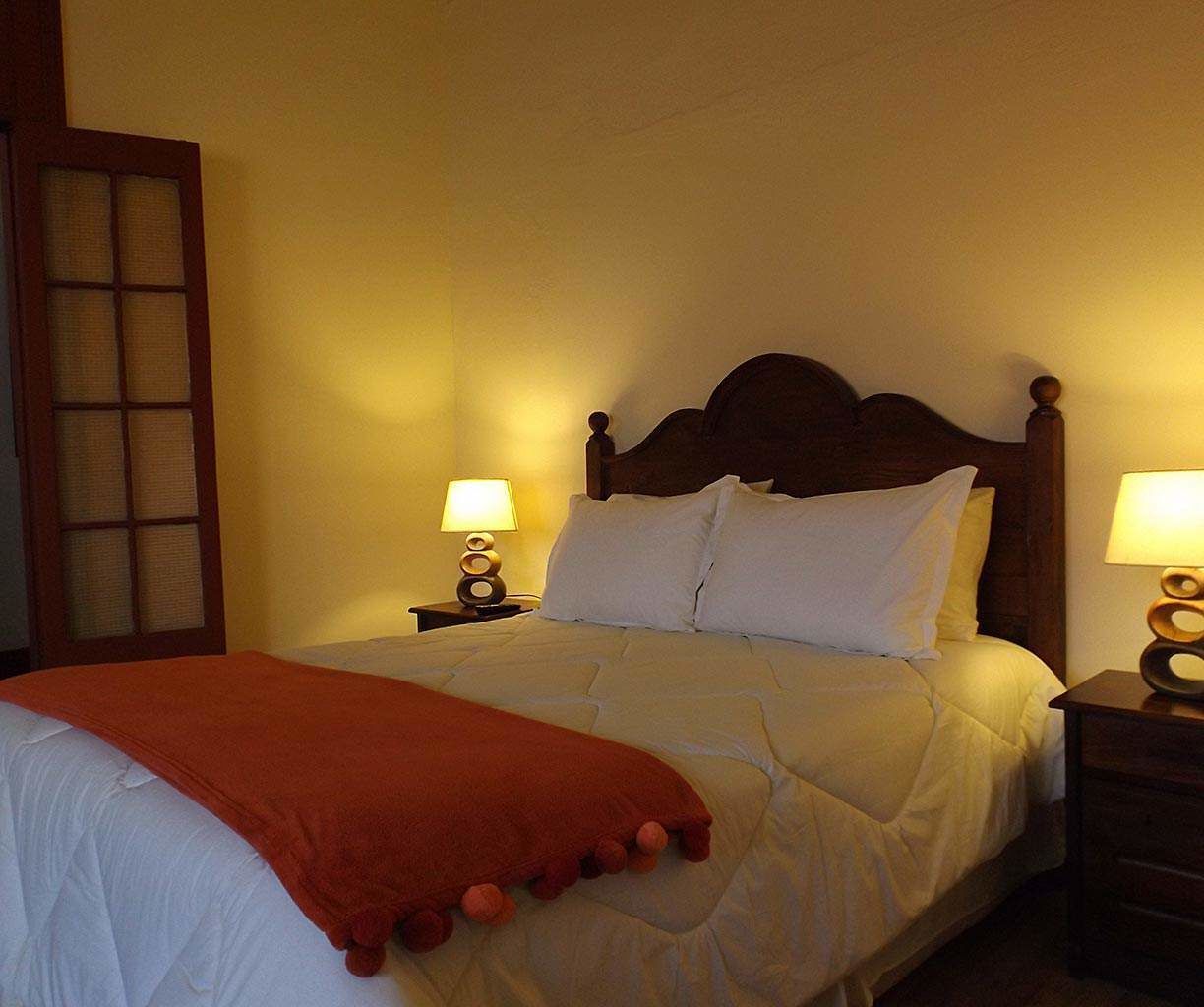 A neatly made bed with white bedding and a red throw blanket, flanked by two bedside tables with lamps.