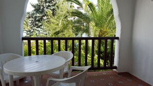 A balcony with a white table and chairs, surrounded by a black railing, overlooking a lush garden with various trees and plants. - Resort Medina del Zoco (Mijas)