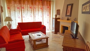 A living room with a red sofa, a glass coffee table, a fireplace, and a television. - Resort Medina del Zoco (Mijas)