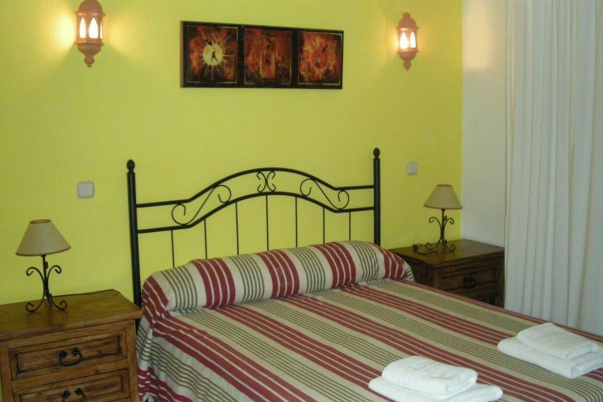 A bed with striped bedding, two bedside tables with lamps, and wall-mounted light fixtures.
