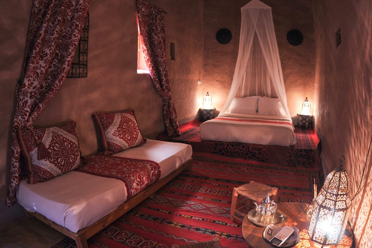 A room with a low bed, a sofa, patterned rugs, and a canopy bed.