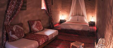 A room with a low bed, a sofa, patterned rugs, and a canopy bed.