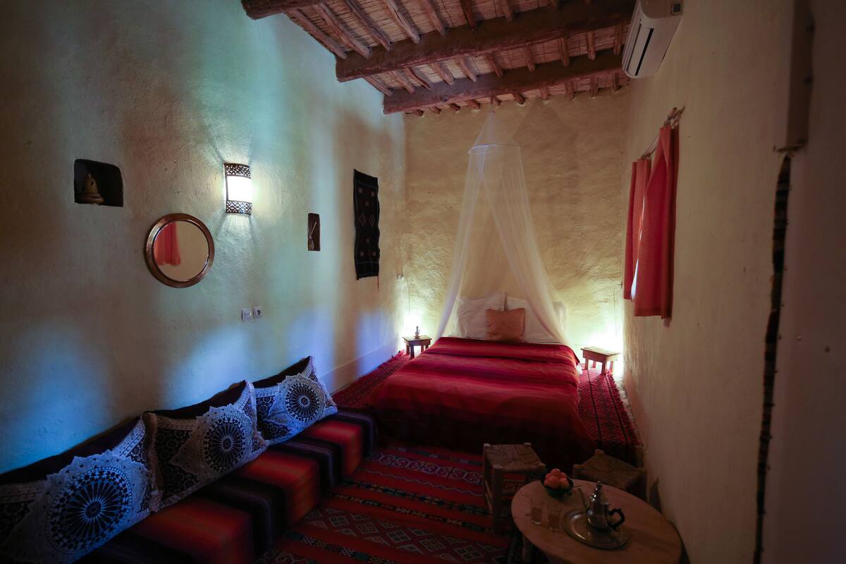 A cozy room with a bed, a sofa, a small table, and a wall-mounted air conditioner.
