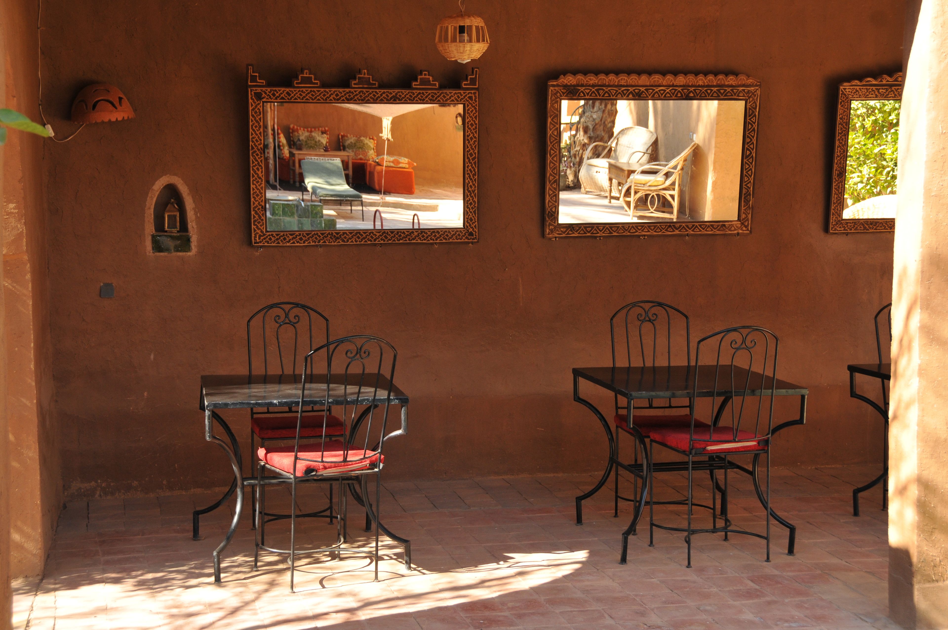 A dining area with two tables and four chairs, each with a red cushion. There are three wall-mounted mirrors with decorative frames.
