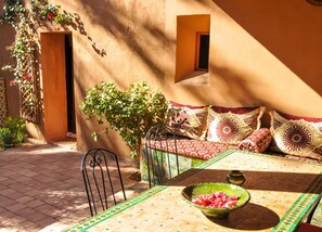 A sunlit patio with a table, chairs, and a sofa with patterned cushions.