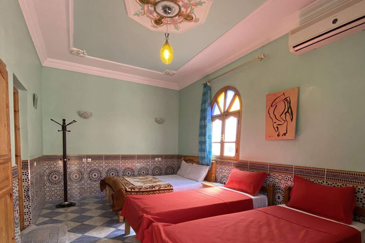 Une chambre avec deux lits, un sol à carreaux, un plafond décoratif et une fenêtre avec des rideaux.