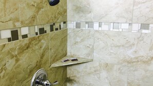 A bathroom with a shower, marble walls, and a tiled shelf. - Relax Inn Lawton (Lawton)