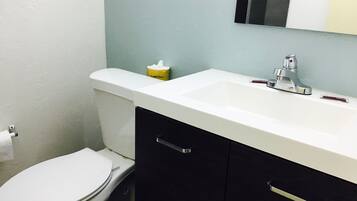 Un baño con inodoro blanco, lavamanos blanco y grifo cromado, y un mueble negro con tirador plateado.