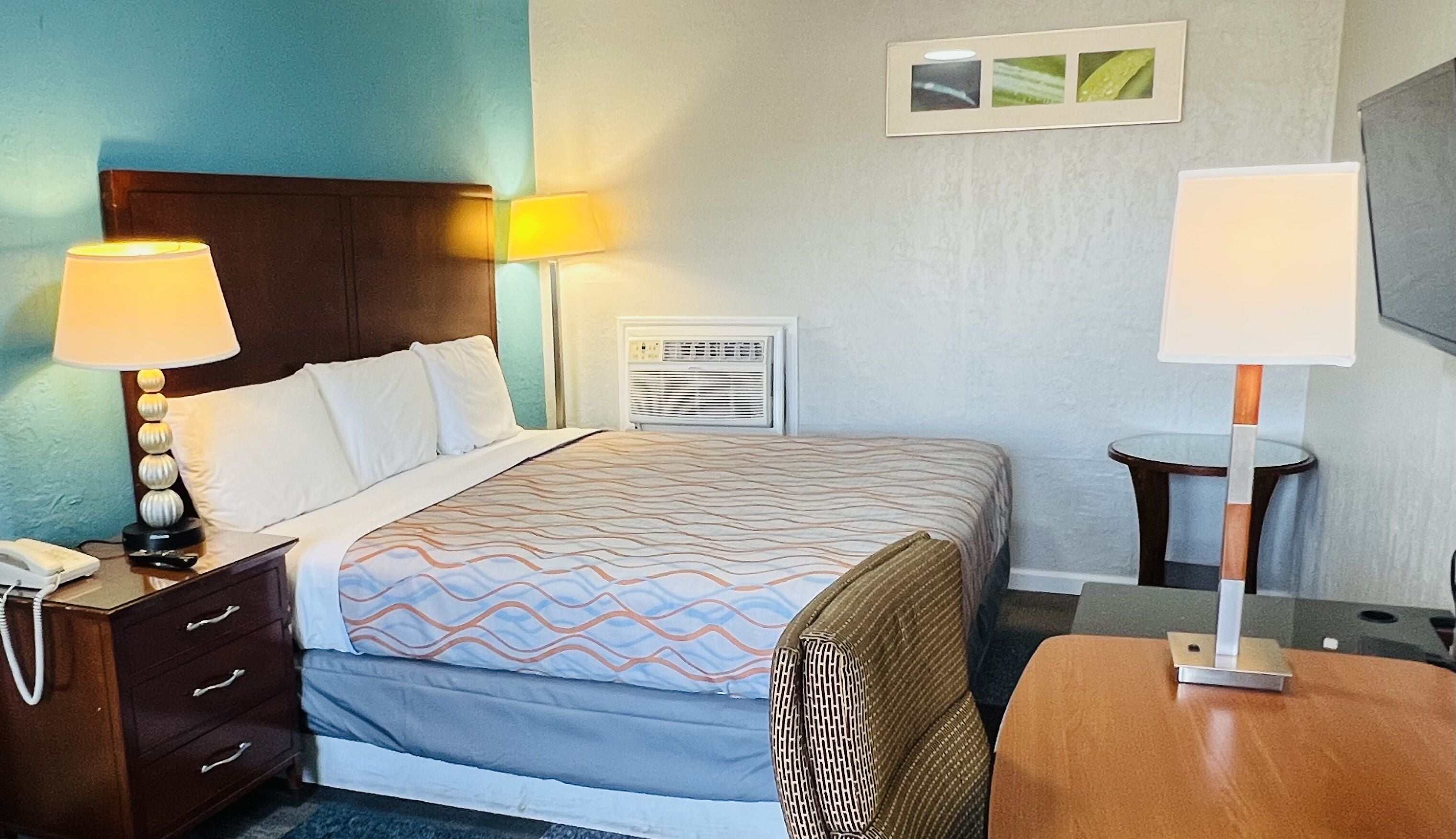 A hotel room with a bed, bedside lamps, a desk, and a small table.