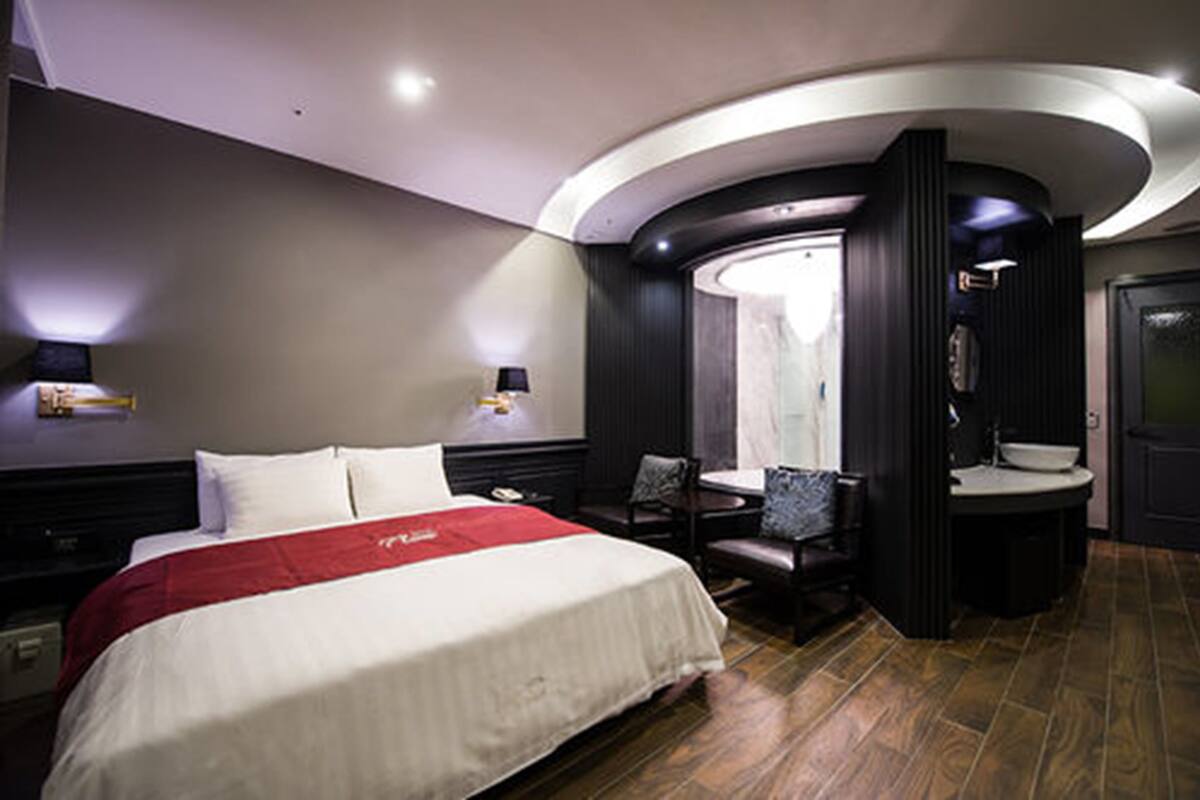 A hotel room with a large bed, a desk, a chair, a round bathroom, and a dark-colored wardrobe.
