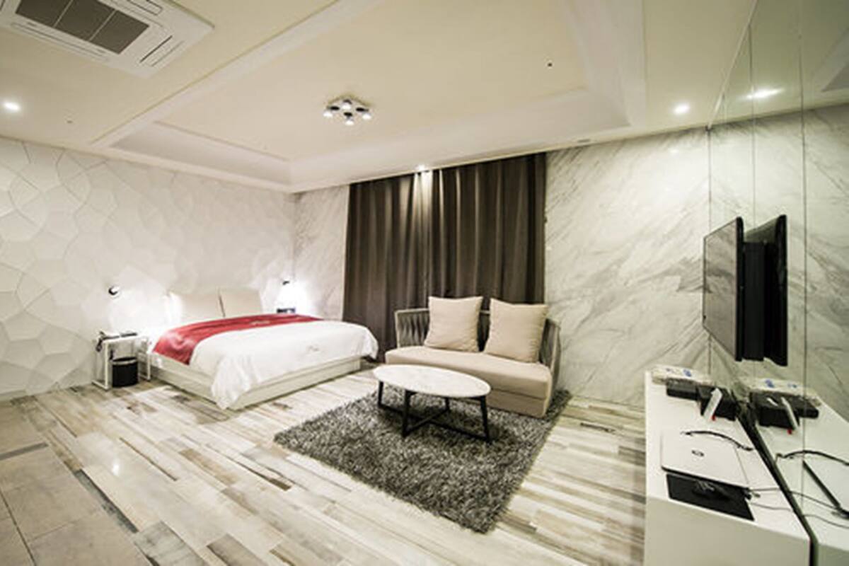 A modern hotel room with a large bed, a sofa, a coffee table, and a TV.