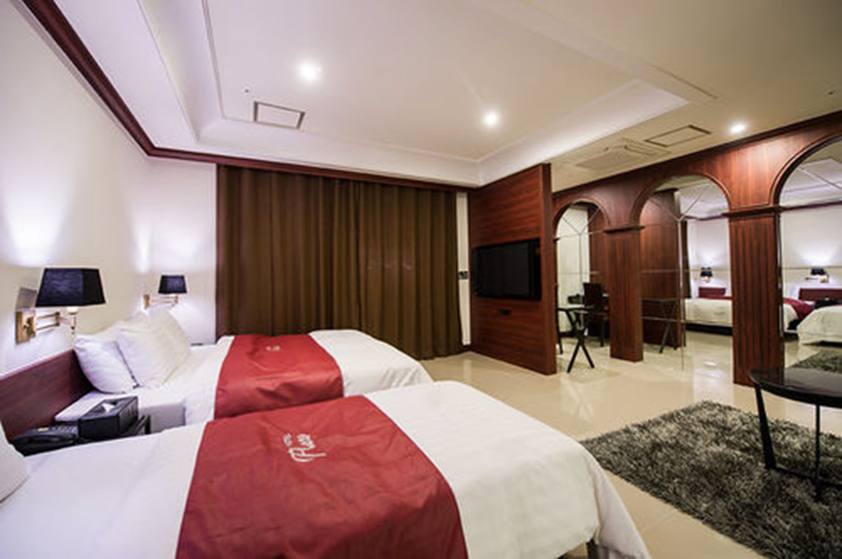 A hotel room with two beds, a television, a desk, and a mirror.