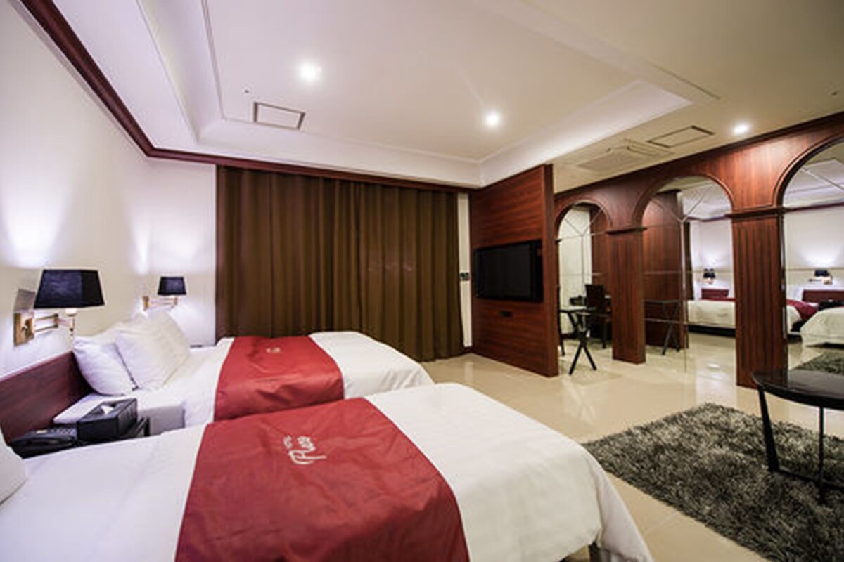 A hotel room with two beds, a television, a desk, and a mirror.