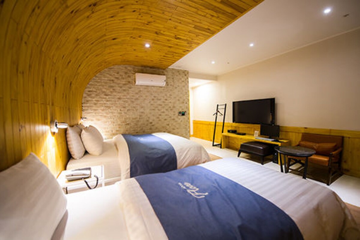 A hotel room with two beds, a television, a desk, and a chair.