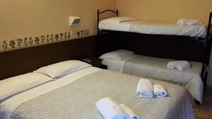 Ett hotellrum med två separata sängar, var och en med ett mönstrat överkast och kuddar. Ovanför sängarna finns en väggmonterad lampa, och längs den nedre delen av väggen löper en dekorativ list med blommönster.
