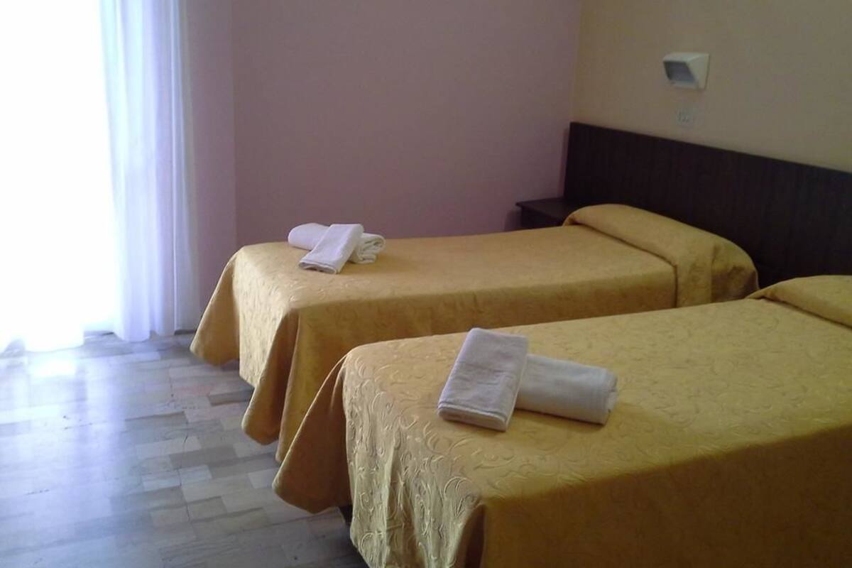 Two single beds with yellow bedspreads and white towels, a wooden floor, and a window with curtains.