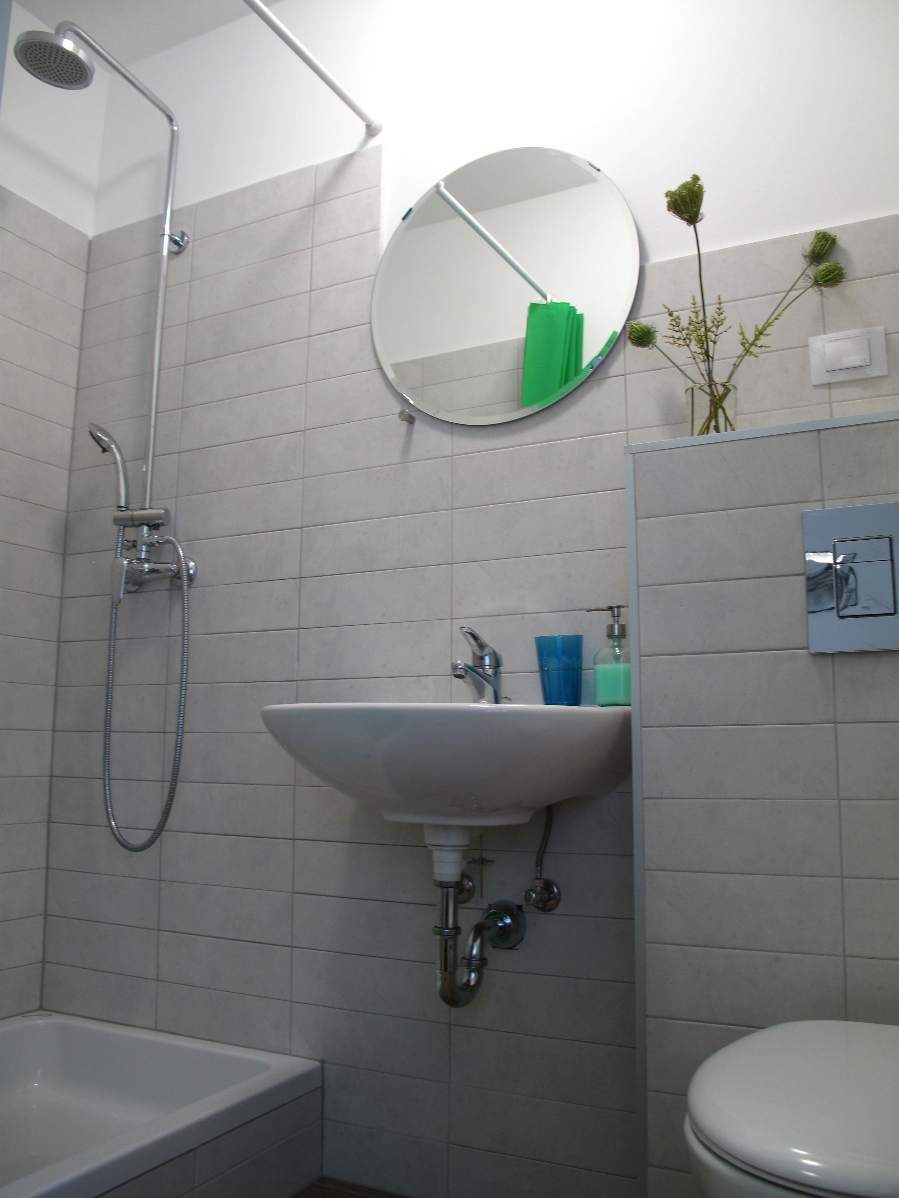 Un baño con bañera, lavabo, inodoro, cabezal de ducha, espejo y una pequeña planta verde en la pared.