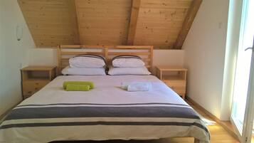 A single bed with two pillows, a green towel, and a white towel.