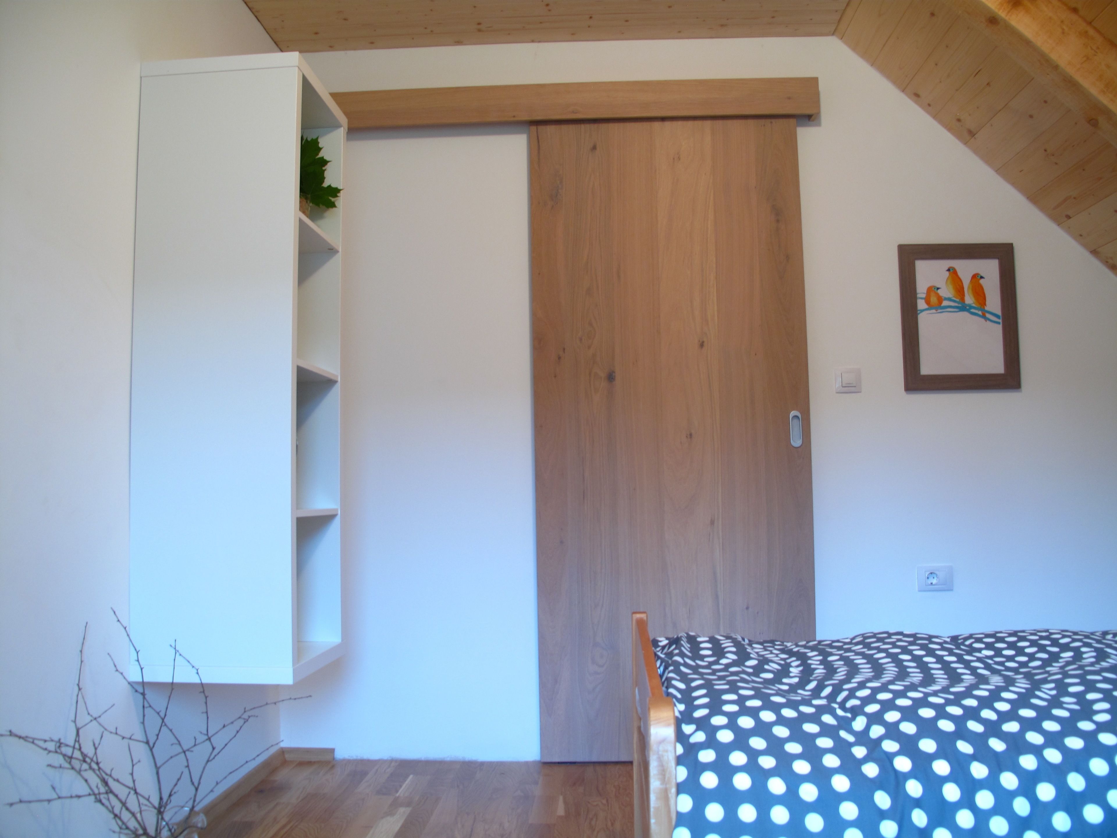 Un dormitorio con una cama, un armario de madera, una estantería blanca y un cuadro en la pared.