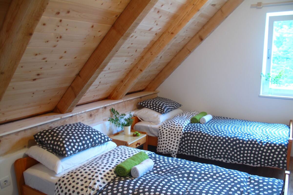 Una habitación pequeña y acogedora con dos camas, cada una con ropa de cama y almohadas a lunares. El techo tiene vigas de madera y una ventana que deja entrar luz natural.